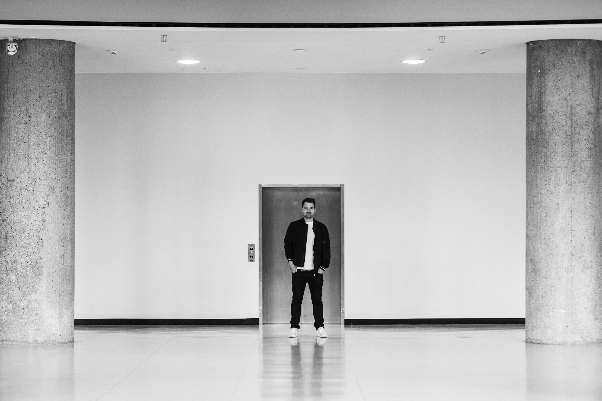 Christian Häringer standing in front of an elevator in a concrete hall, a large wall clock above him